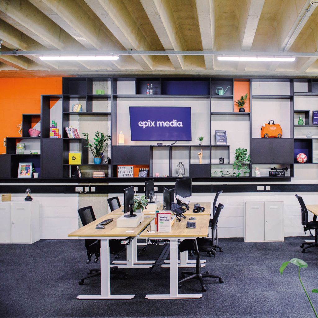 The Epix Studio showing our large shelving until containing lots of trinkets, books and lights, with 4 of our height adjustable desks